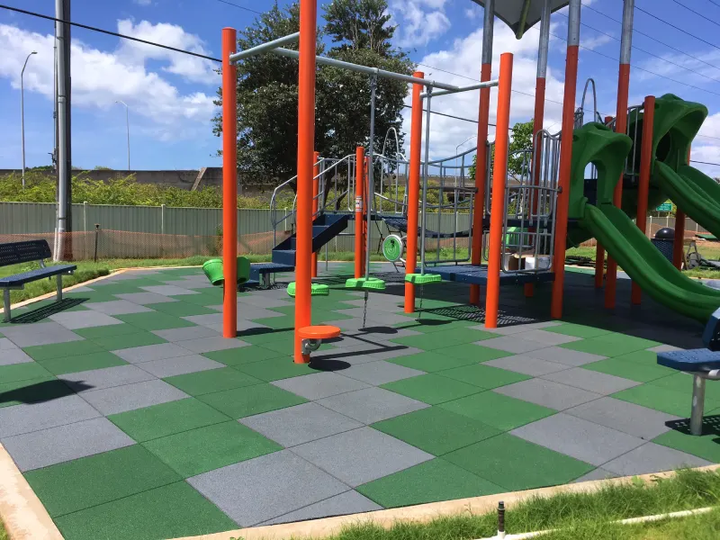 A modern playground with colorful play equipment installed on a surface of green and grey rubber flooring tiles.