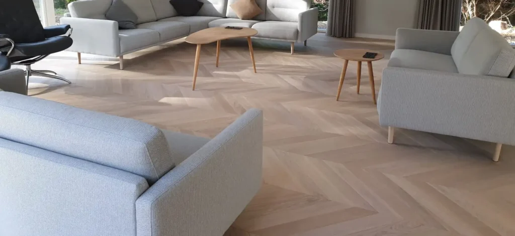 living room featuring light-colored chevron wood flooring, with a light gray sectional sofa